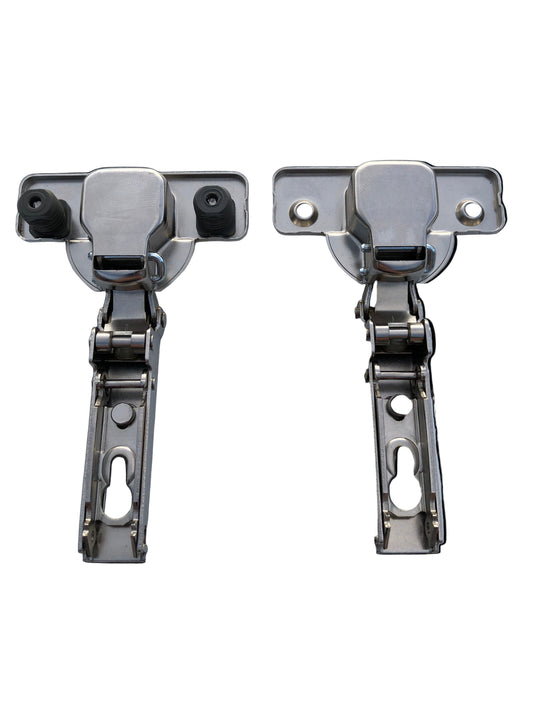Two cabinet hinges with attached screws and dowels on a clear surface.